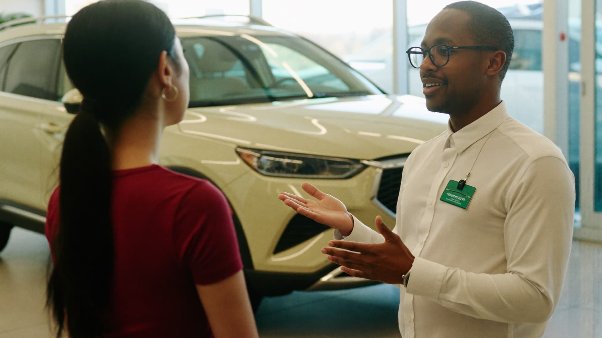 A car salesperson listening to a customer beside an SUV in a dealership showroom