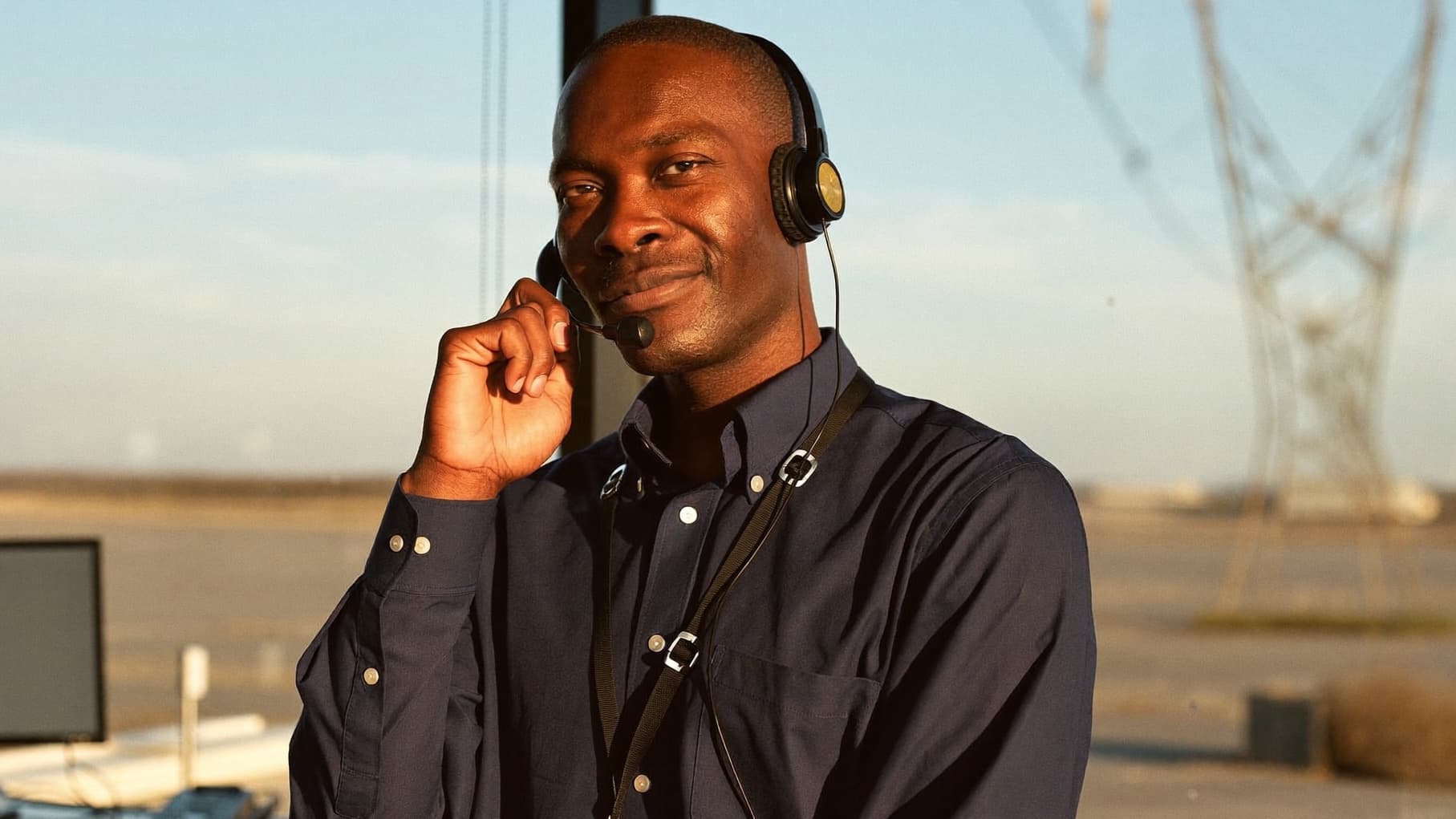An energy broker on a headset call at a window at golden hour, transmission towers in the distance