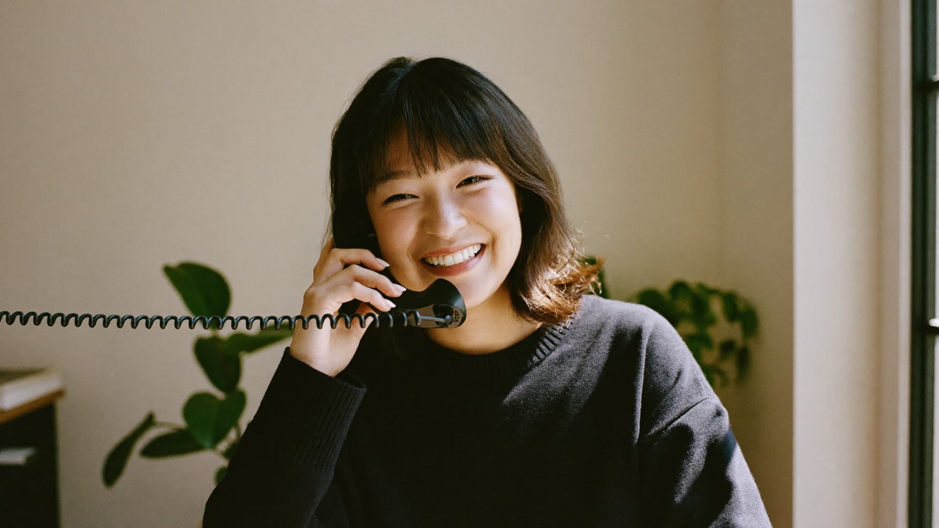 An inside-sales rep smiling on a phone call by a sunlit window